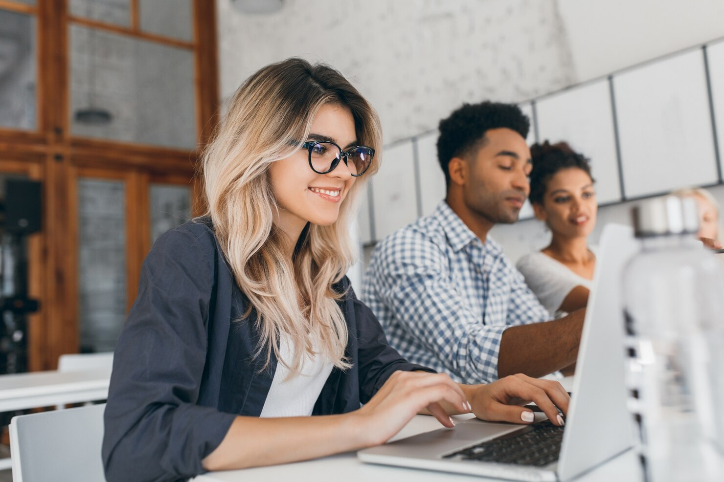 A woman facing an open laptop and typing while two co-workers review one of their screens in the background.